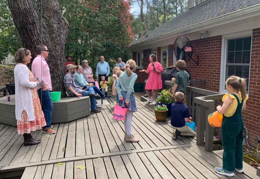 Neighbors gather on the wooden back deck of a brick house.